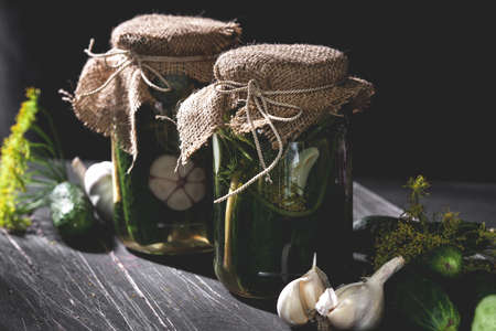 Two jars of pickled cucumbers with garlic and dill on black tableの写真素材