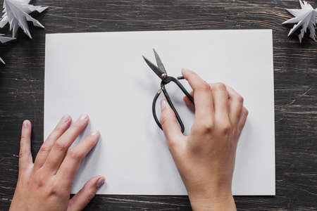 Sheet of paper with hands holding scissors on the black wooden tableの写真素材