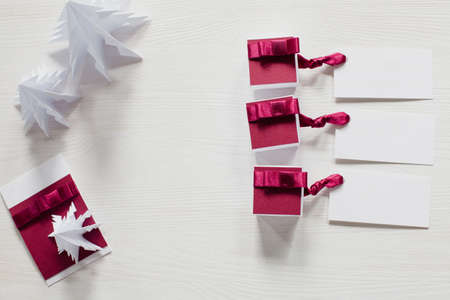 Origami trees and small gift boxes with labels on white table, top view