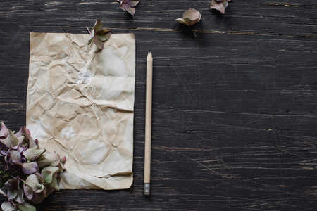 Rustic sheet of paper with pencil and hydrangea flowers on black wooden tableの写真素材