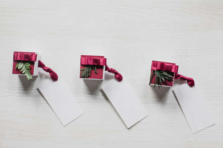 Three gift boxes with labels on white, wooden table, flat lay