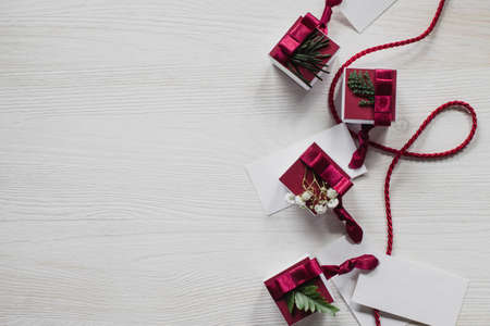 Christmas gifts with labels and spruce decorations on white wooden table and burgundy ribbon and origami treesの写真素材