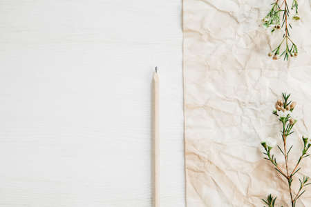 Old paper and pencil with little white flowers on the side of white wooden tableの写真素材