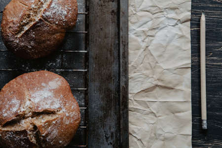 Freshly baked bread lying on cooling rack and scratched wooden table with paper and pencilの写真素材
