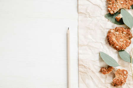Healthy oat cookies on the white wooden table with paper, pencil and eucalyptus leavesの写真素材