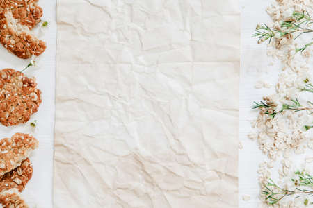 Healthy oat cookies on the side of white wooden table with paper and flowersの写真素材