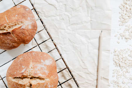 Round homemade bread on cooling rack with piece of paper, pencil and oatsの写真素材