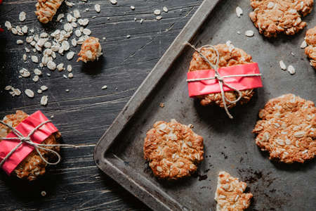 Anzac cookies on a black metal tray with red flowers on wooden tableの写真素材