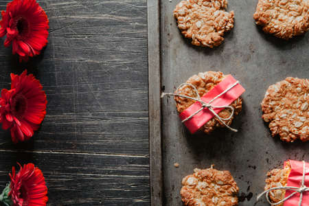 Anzac cookies on a black metal tray with red flowers on the side の写真素材