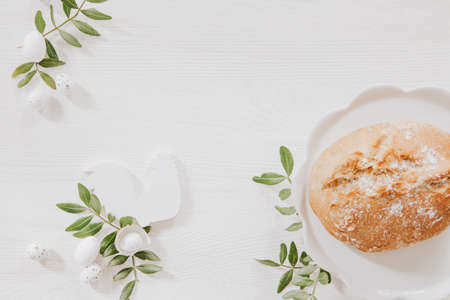 Natural Easter decoration with white wood and green leaves on wooden table with bread on white plateの写真素材