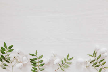 White and green Easter decoration with flowers, leaves and little eggs on white wood, flat layの写真素材