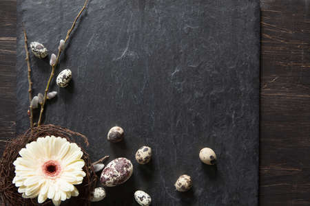 Simple easter decoration with eggs, yellow gerbera flower in a wreath and fluffy willow on dark stoneの写真素材