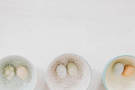 Beautiful pastel eggs in decorative bowls on the bottom of white wooden backgroundの写真素材