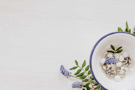 Simple Easter decoration with eggs in a bowl and grape hyacinths in the corner of white wooden backgroundの写真素材
