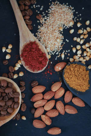 different spoons filled with spices and grains, you will find nuts, curry, paprika, coffee, corn, sunflower seeds on a black background.の写真素材