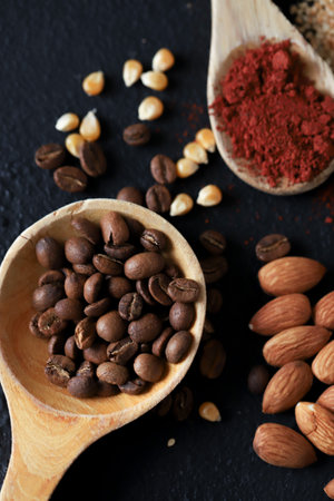 different spoons filled with spices and grains, you will find nuts, curry, paprika, coffee, corn, sunflower seeds on a black background.の写真素材