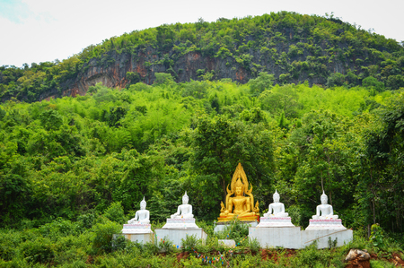 buddha statue on hill / white and yellow buddha statue on green mountain with tree backgroundの写真素材