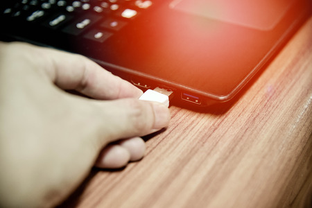 hand plugging usb cable in notebook device / white electronics cable in usb port on computer accessoriesの写真素材