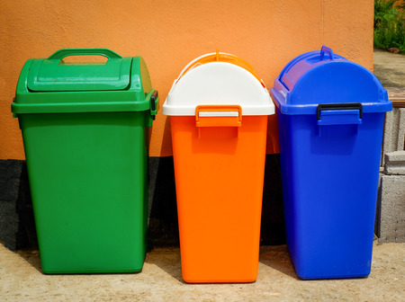 colorful bin outdoors / close up of recycle bins stand on wall - green orange and blue bin various sizes in the garden parkの写真素材