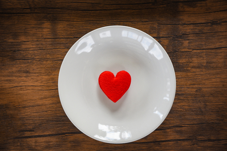 Valentines dinner romantic love food and love cooking concept / Red heart on white plate romantic table setting decorated with red heart wooden rustic texture backgroundの写真素材