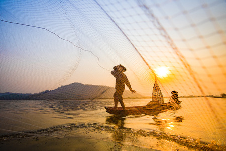 Fisherman on boat river sunset / Asia fisherman net using on wooden boat casting net sunset or...