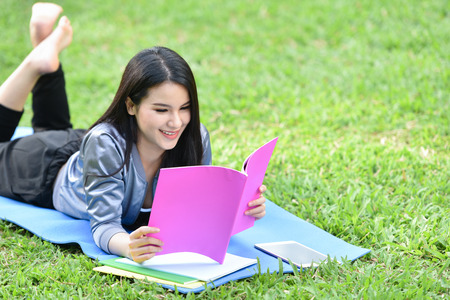 Women read book outdoors in the garden park / smiling young girl lying in grass field read books...