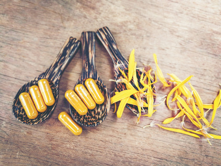 Herbal medicine nature - Natural Extract turmeric for herb medicine capsules on wooden spoon - Yellow capsules with petals sunflowe on wood backgroundの写真素材