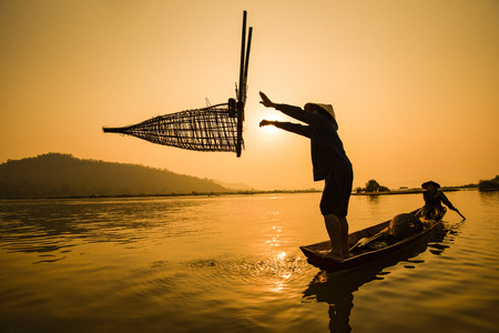Fisherman on boat river sunset / Asia fisherman bamboo fish trap on wooden boat sunset or sunrise in the Mekong river - Silhouette fisherman boat with mountain background life person countrysideの写真素材