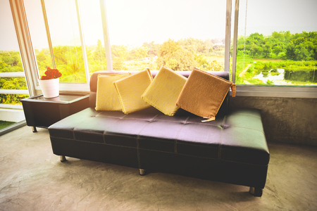Sofa in the morning room sunlight through open window / Black sofa pillow by the window glass home looking out nature backgroundの写真素材