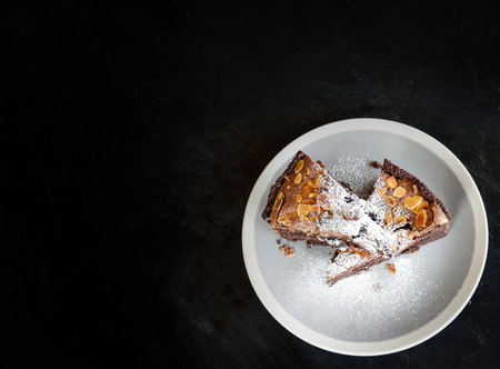 brownies cake on the table / piece of chocolate cake cocoa with nut and icing sugar on top view brownies slice on white plate the wooden dark backgroundの写真素材