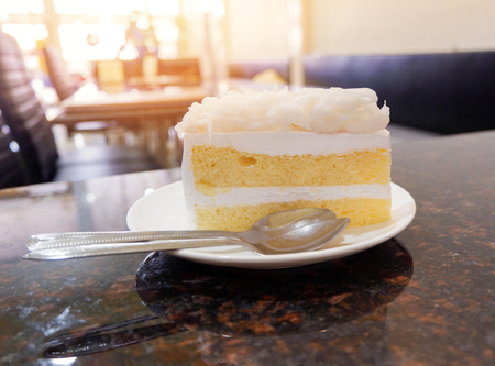 Cake slice on white plate with coconut cake milk dessert and spoon on table in the coffee shopの写真素材
