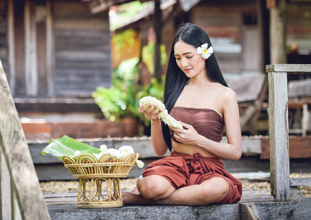 Asia woman drama style dress Sitting on old thai house / Portrait of beautiful young girl smiling traditional costume wearing with thai jasmine garland in handの写真素材