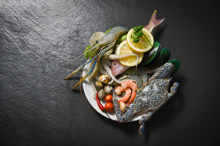 Shellfish seafood plate with shrimps prawns crab shell cockles mussel squid and fish ocean gourmet dinner / Fresh raw seafood with herbs and spices lemon on dark backgroundの写真素材