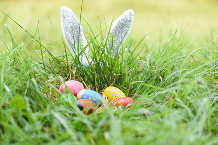 Easter bunny and Easter eggs on green grass outdoor / Colorful eggs in the nest and ear rabbit on field spring meadowの写真素材