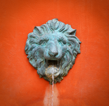 Face statue lion head on orange wall - fountain water flow from mouth lion statueの写真素材