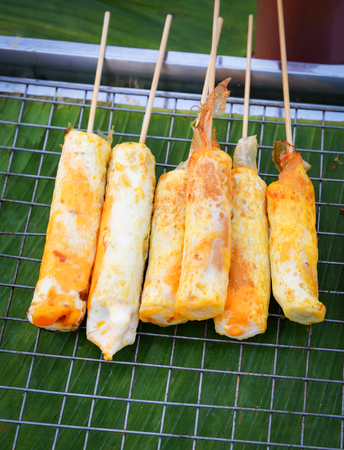 Sausage and hot dog roll wrapped with eggs cooking on grill at street food marketの写真素材