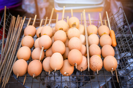 Eggs grilled with bamboo stick on grill hot stove in street food market thailand / egg seasoningの写真素材