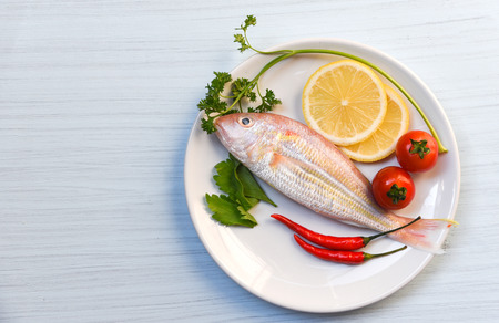 Seafood fish plate lemon parsley chilli and tomato on white plate table background top view