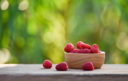 Fresh raspberry in wooden bowl / Close up red raspberries fruit and nature green blur background