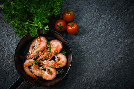 Seafood plate with shrimps prawns cooked on pan with herbs and spices lemon tomato and curly parsley on dark backgroundの写真素材