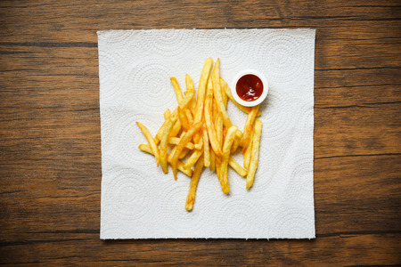 French fries on white paper with ketchup on wooden background