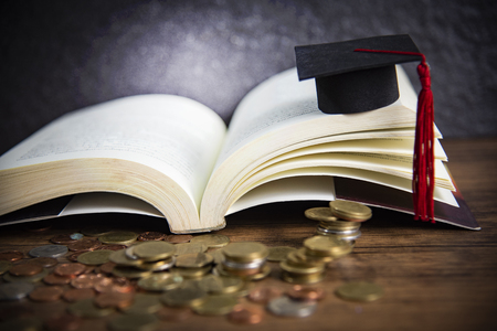 Scholarship for education concept with money coin on wooden with dark background and graduation cap on a open bookの写真素材