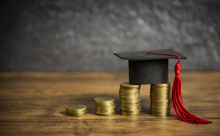 Scholarships education concept with graduation cap on coin money saving  for grants education on wooden table dark backgroundの写真素材