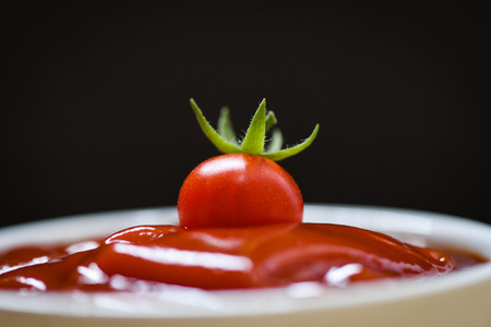 Fresh tomato on ketchup and dark background / Close up tomato sauce in cup - selective focusの写真素材