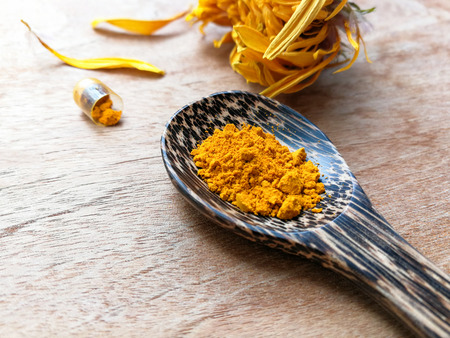 turmeric powder natural herbs on wooden spoon with capsule and yellow flower on wood table backgroundの写真素材
