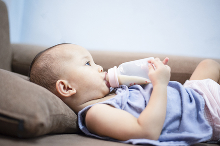 baby feeding bottle / Closeup portrait of asia child hold milk bottle and feeding on sofa bedの写真素材