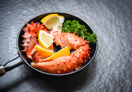 Boiled crab claws cooked seafood pan with Alaskan King Crab with lemon parsley herbs and spices on dark background / red crab hokkaido in a hot potの写真素材