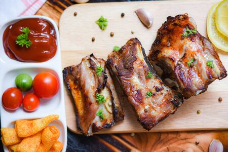 bbq pork ribs grilled with tomatoes ketchup and herbs spices served on the wooden cutting board on table / Roasted barbecue pork spare rib slicedの写真素材