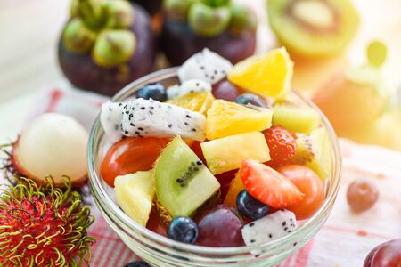 Fruit salad bowl fresh summer fruits and vegetables healthy organic food strawberries orange kiwi blueberries dragon fruit tropical grape pineapple tomato lemon mangosteen rambutan backgroundの写真素材