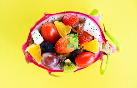 Fruit salad bowl served in a dragon fruit and vegetables healthy organic food strawberries orange kiwi blueberries grape pineapple tomato lemon fresh summer fruits tropical on yellow backgroundの写真素材